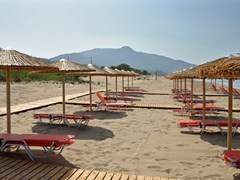 small-Straw umbrellas and rows of lounge sunbed chairs at sandy beach in Greece.